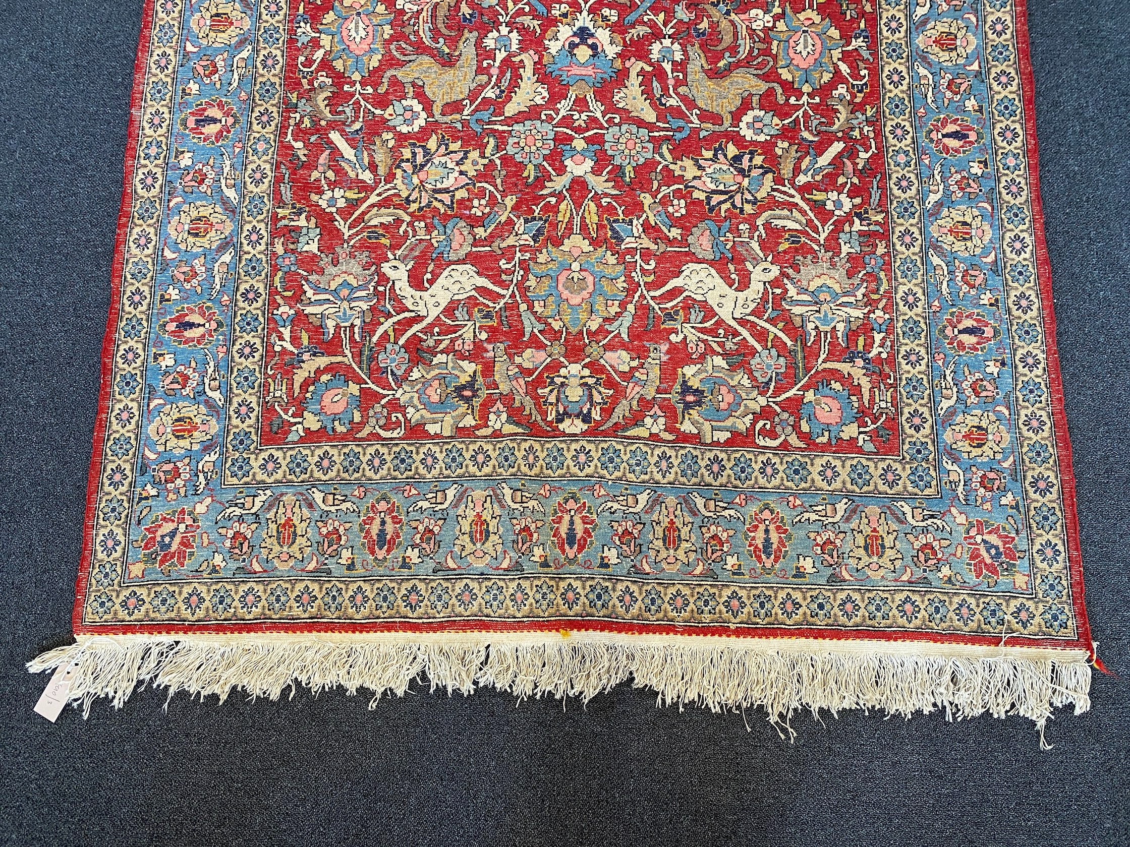 A Persian Qum red ground rug woven with animals and exotic birds among stylised flower heads 220 x 125 cms